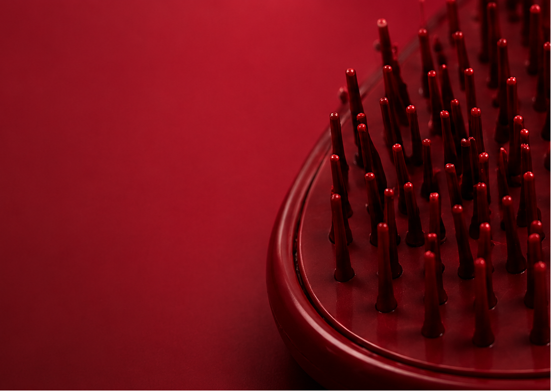 Red hairbrush with bristles against a red background